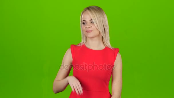 Dívka v červené barvě na zeleném pozadí ukazuje její ruku — Stock video