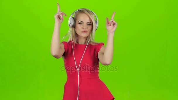 Blondes Mädchen in rotem Kleid, das mit Kopfhörern tanzt, grüne Leinwand — Stockvideo