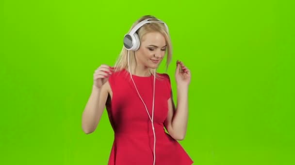 Сексуальная девушка в красном платье танцует в наушниках, зеленый экран — стоковое видео