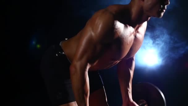 Bodybuilder gör övningar med en skivstång. Svart rök bakgrund. Slow motion — Stockvideo