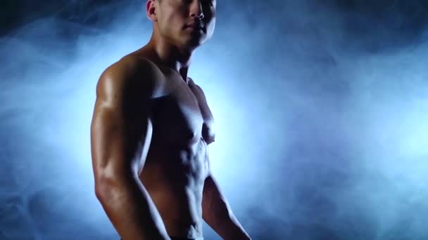 asiatischer muskulöser Mann demonstriert seinen Körper, seine Kraft und Ausdauer. schwarzer Rauchhintergrund. Zeitlupe