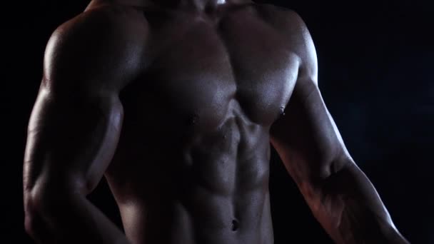 Bodybuilder dimostra il suo corpo, la forza e la resistenza. Fondo nero fumo. Al rallentatore. Da vicino. — Video Stock