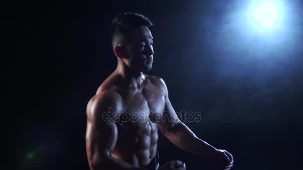 Homem muscular asiático demonstra o corpo inflado, ele é forte. Fundo preto. Movimento lento — Vídeo de Stock