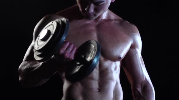 Asian bodybuilder training biceps with a dumbbells. Black smoke background. Slow motion — Stock Video