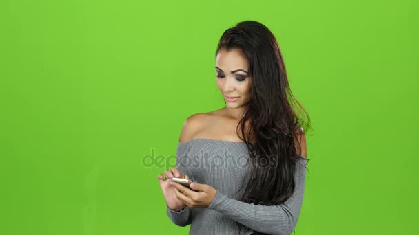 Brunette vrouw met glimlach speelt op mobiel, groene schermachtergrond — Stockvideo
