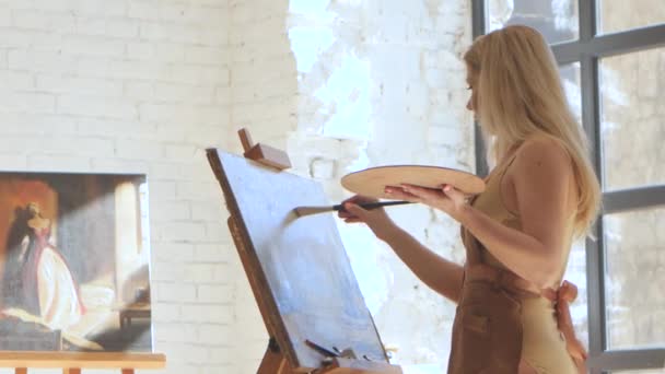 Mujer artista pinta sobre lienzo amplio cepillo y sostiene paleta — Vídeos de Stock