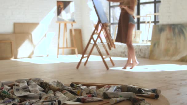 Дівчина малює картину з олією стоїть босоніж на підлозі студії — стокове відео