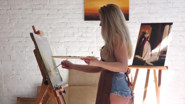 Kvinnlig konstnär står nära staffli målning på duk med olja — Stockvideo