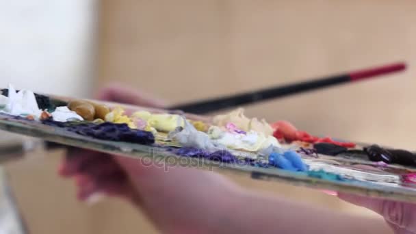 Primer plano, paleta con colores de pintura al óleo en la mano artista — Vídeo de stock