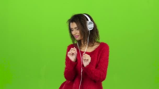 Dança feminina e sorri com fones de ouvido, tela verde. Movimento lento — Vídeo de Stock