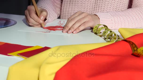 Руки дизайнера рисует эскиз платья, на тканевом столе, для пошива. Закрыть — стоковое видео
