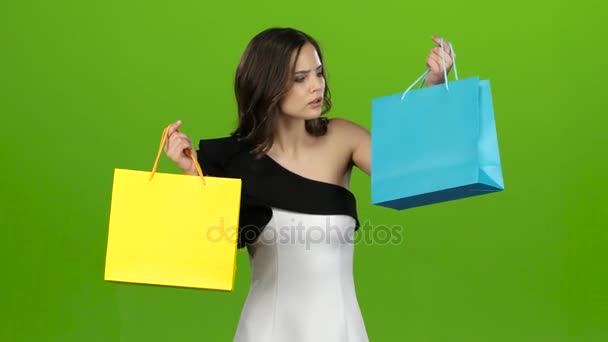 Flickan håller shoppingkassarna och tvivel vad du ska välja. Grön skärm — Stockvideo