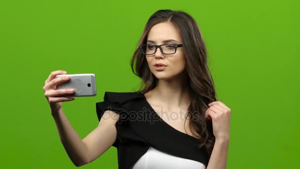 Девушка со смартфоном в руках делает селфи. Зеленый экран — стоковое видео