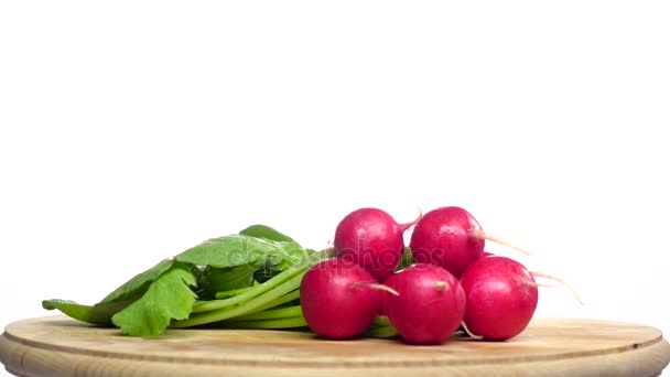 Bunch of radishes are spinning on a wooden board. White background — Stock Video