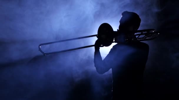 Человек в центре внимания в дымчатой студии играет на тромбоне, силуэте — стоковое видео