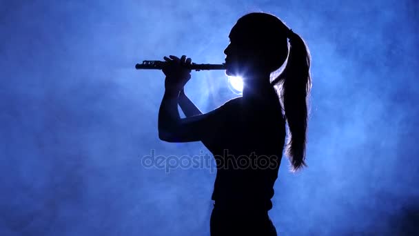 Woman in spotlight in smoky studio plays on flute, silhouette — Stock Video