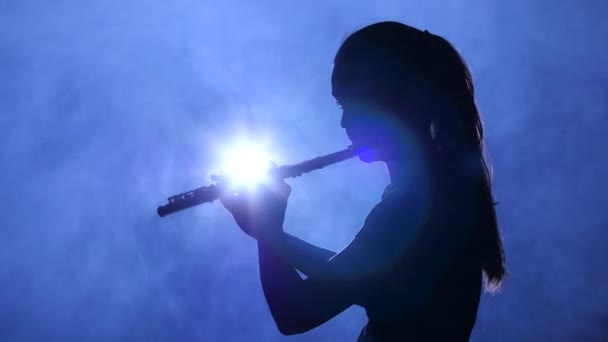 Weibchen im Rampenlicht im verrauchten Atelier spielt auf Flöte, Silhouette — Stockvideo