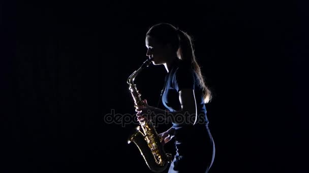 Жінка-музикантка, що грає на саксофоні стоїть збоку на чорній студії — стокове відео