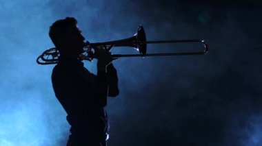 Siluet trombonunu oynayan adam. Dumanlı stüdyo, ağır çekim