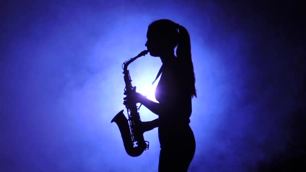 Vrouw in rokerige studio speelt op saxofoon, silhouet. Slow motion — Stockvideo