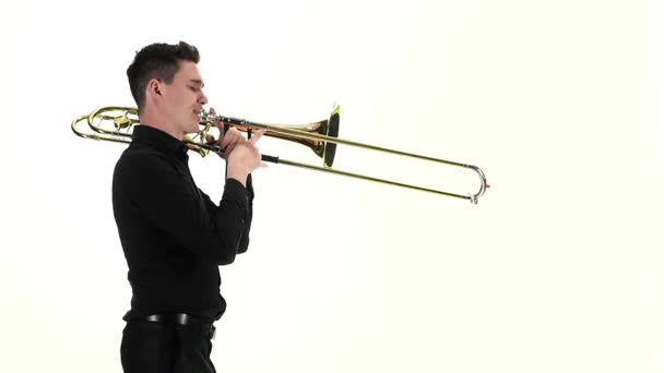 Молодой музыкант играет на тромбоне стоя боком в замедленной съемке — стоковое видео