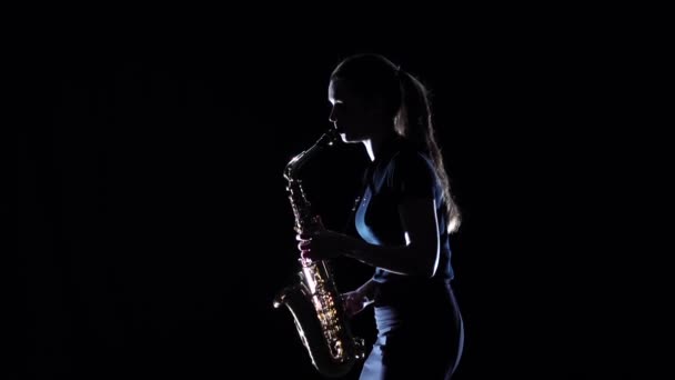 Брюнетка грав на саксофоні стоячи вбік. Повільний рух, чорний студії — стокове відео