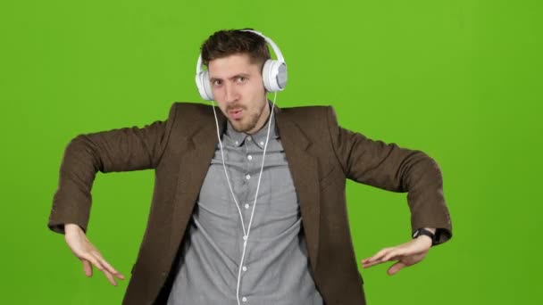 Man luistert naar muziek via de koptelefoon, dansen en bouwt grimaces. Groen scherm — Stockvideo