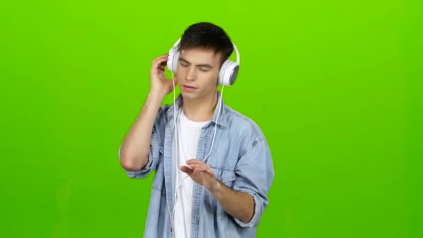 Guy escucha la música en los auriculares y se ajusta a lo positivo. Pantalla verde — Vídeos de Stock