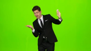 İşadamı yürür, bir not defteri başparmak ve bir selfie yapar. Yeşil ekran. Yan görünüm