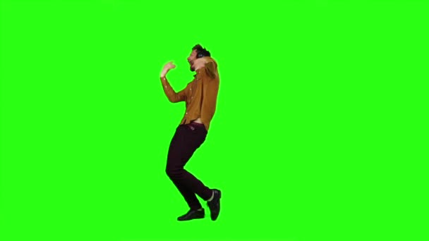 El hombre con auriculares escucha música, baila y canta una canción. Pantalla verde. Movimiento lento — Vídeo de stock