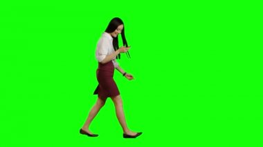 Kız yürüyor ve bir telefon tutar ve fotoğraflara görünüyor. Yeşil ekran. Yan görünüm