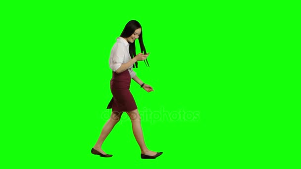 Κορίτσι βόλτες και κατέχει ένα τηλέφωνο και φαίνεται στις φωτογραφίες. Πράσινη οθόνη. Πλάγια όψη — Αρχείο Βίντεο
