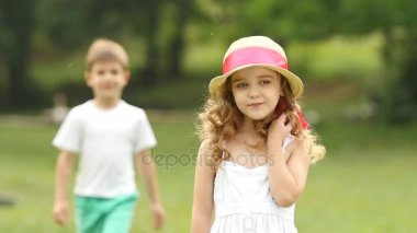 Küçük kız parkta duruyor, onun arkasında küçük bir çocuk. Ağır çekim