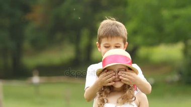 Küçük çocuk, kendi elleriyle gözlerini kıza kapatır. Ağır çekim