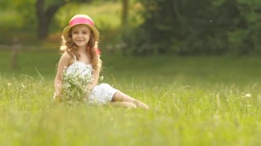 Bebek sarafan ve şapka glade oturur, kır çiçekleri ve gülümsüyor tutar. Ağır çekim