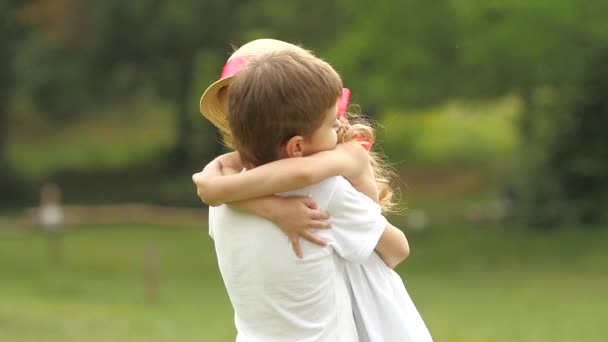 El niño toma a la niña en sus brazos y ellos giran en el parque. Movimiento lento — Vídeos de Stock