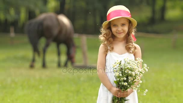 Klein meisje staat in een park met een boeket van wilde bloemen. Slow motion — Stockvideo