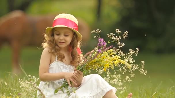 Ребенок сидит на поляне, переворачивает разорванные дикие цветы и делает из них букет. Медленное движение — стоковое видео