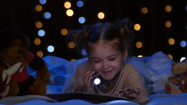 La niña lee un libro en manos de un fanático por la noche y se ríe. Fondo de Bokeh — Vídeo de stock