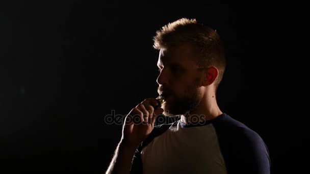 O homem segura um cigarro eletrônico na mão, inala e exala muita fumaça. Fundo preto — Vídeo de Stock