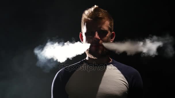 Άντρας καπνίζει ένα ηλεκτρονικό τσιγάρο, Απολαύστε τη στιγμή. Μαύρο φόντο — Αρχείο Βίντεο