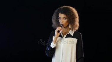 Kız Afro-Amerikan görünüm bir e-sigara içiyor. Siyah arka plan