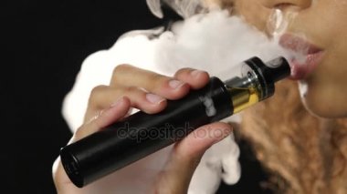 Kız bir nefes alır ve elektronik sigara dumanı exhales. Siyah arka plan. Yakın çekim