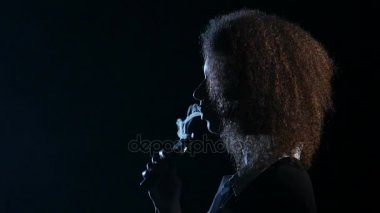 Afrikalı-Amerikalı kadın bir e-sigara içiyor ve ağzına sigara içmek sağlar. Siyah arka plan.