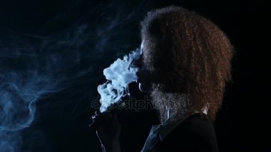 Kız Afro-Amerikan görünüm elektronik sigara içiyor. Siyah arka plan. Yan görünümü. Siluet. Ağır çekim