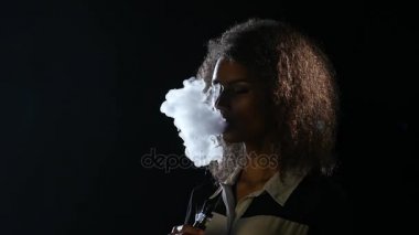 Afro-Amerikan kız boş bir odada elektronik sigara içiyor. Siyah arka plan. Ağır çekim