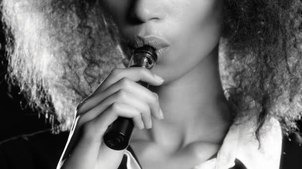 Les lèvres d'une fille d'apparence afro-américaine fument une cigarette électronique. Fond noir. Gros plan — Video