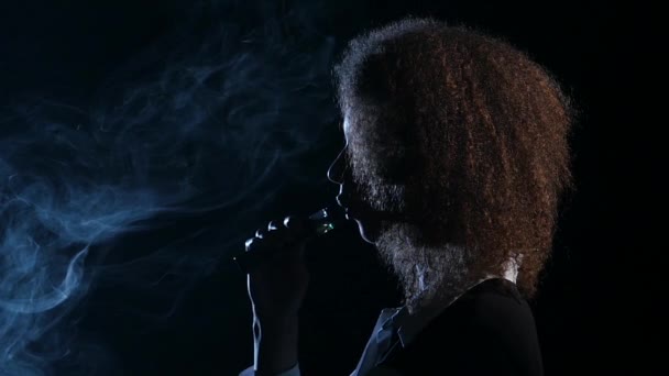 Dziewczyna z african american wygląd pali elektroniczny papieros. Czarne tło. Widok z boku. Sylwetka. Zwolnionym tempie — Wideo stockowe