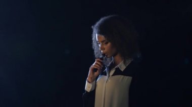 Boş odada Afrikalı-Amerikalı kadın vape serbest bırakır. Siyah arka plan