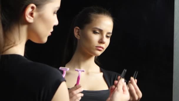 Girl is holding a shaving machine and she is upset with tweezers. Black background — Stock Video